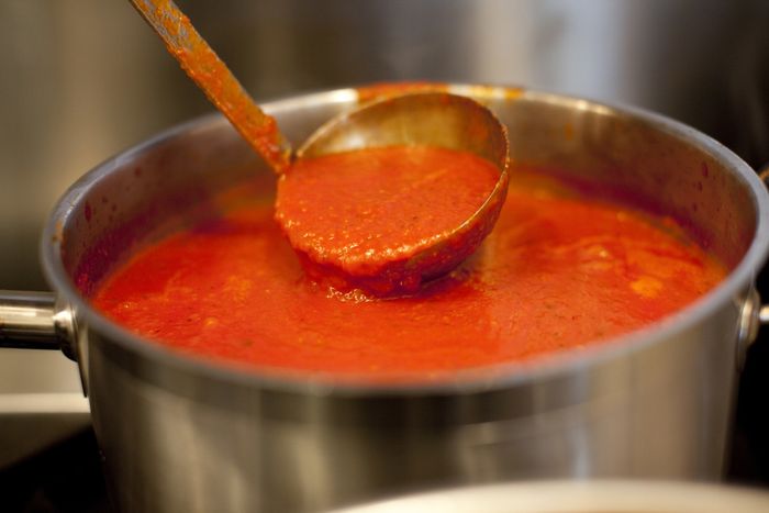 A ladle scooping marinara sauce from a pot.