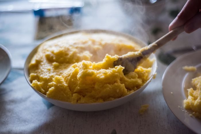 A close-up of a wooden spoon scooping polenta from a plate on a dining table.