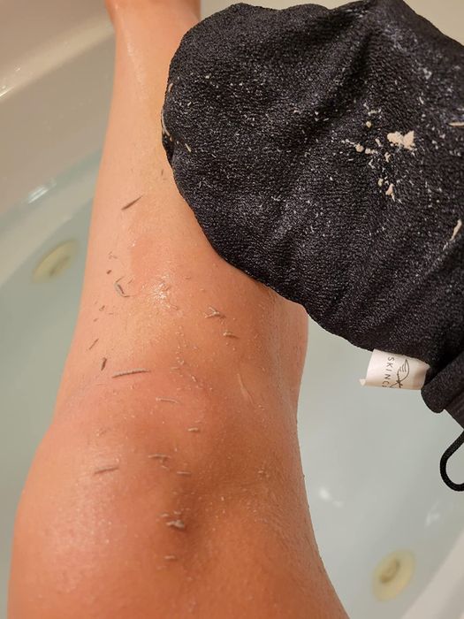 A reviewer demonstrates the exfoliating glove in action, showcasing the dead skin removed from their leg and the glove itself
