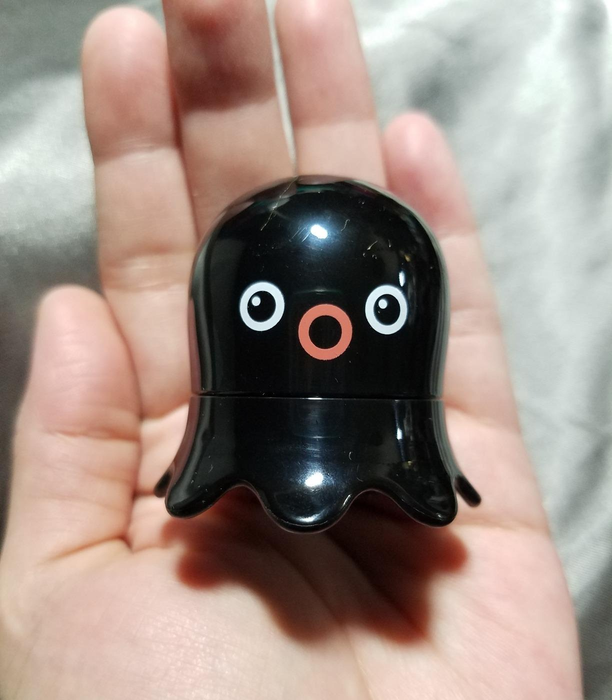 A reviewer holding a small, black, octopus-shaped container with a cute, simple face design