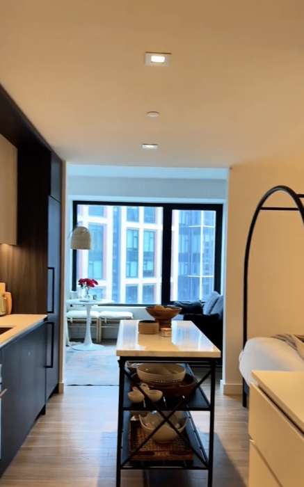 A contemporary studio apartment interior featuring a kitchen, a spacious window, and a stylish floor lamp
