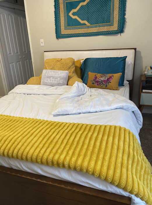 A well-made bed adorned with vibrant pillows, a yellow throw blanket, and a decorative tapestry on the wall