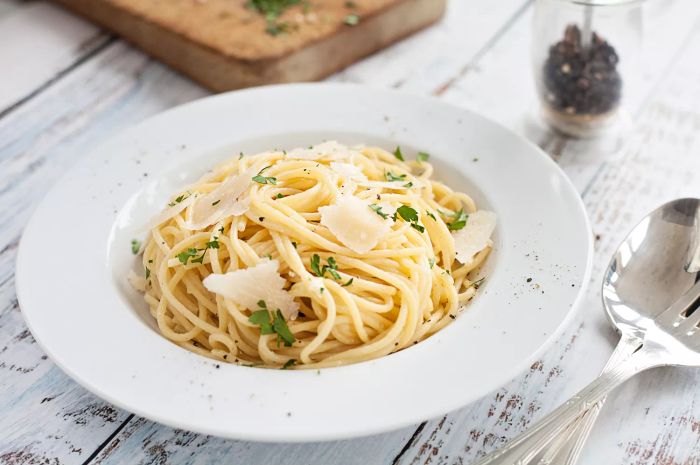 A close-up shot of buttered spaghetti garnished with parmesan cheese, pepper, and fresh parsley