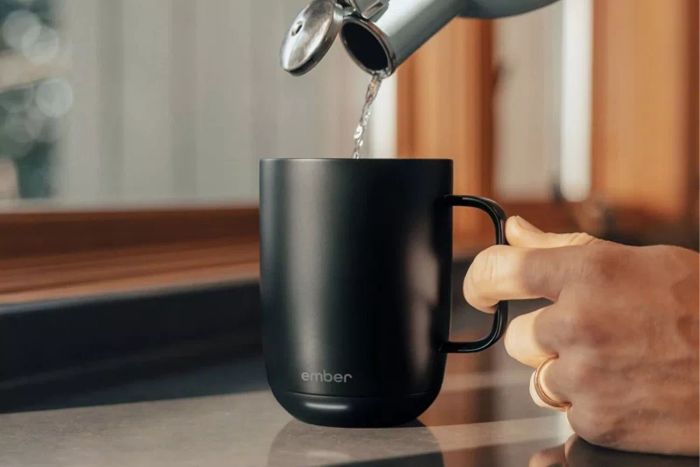 A person pouring hot water from a tea kettle into the Ember Mug 2