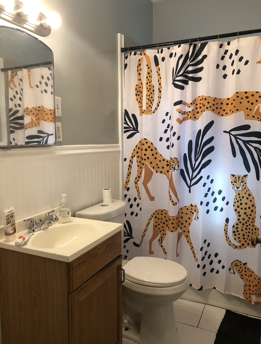 A bathroom equipped with a wooden vanity, a sink, a toilet, and a shower curtain decorated with multiple cheetah prints