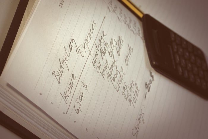 A notebook filled with handwritten budget notes and a calculator placed beside it