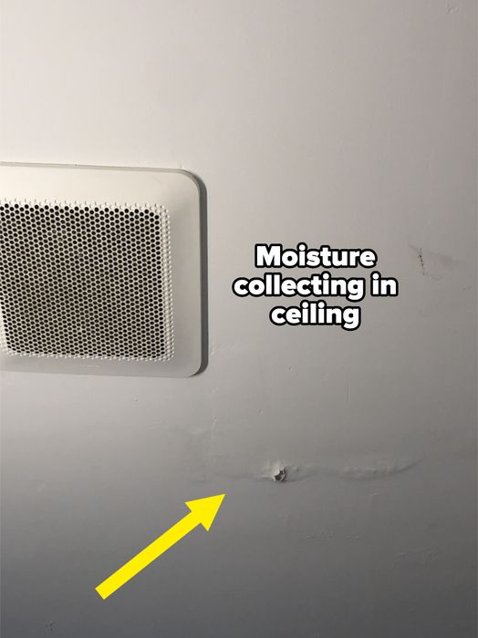 A ceiling showing a ventilation cover, a small hole, and signs of water damage