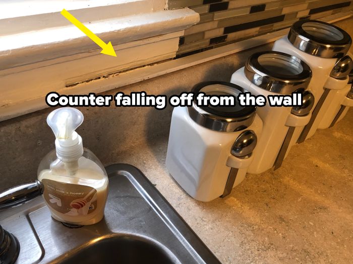 A kitchen countertop featuring four white storage canisters lined up neatly, with a bottle of hand soap placed beside the sink