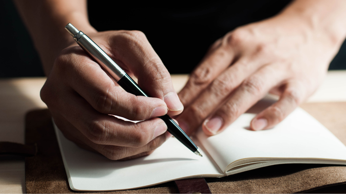 A close-up of hands holding a pen, writing notes in a journal