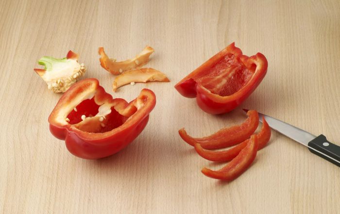 A red bell pepper cored and sliced into strips using a kitchen knife