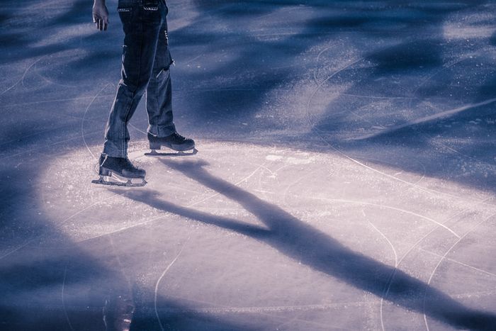 A person is skating on the ice rink, their figure casting a long shadow. They're wearing jeans and skates, and the focus is on their motion, with a dynamic and lively atmosphere surrounding them.
