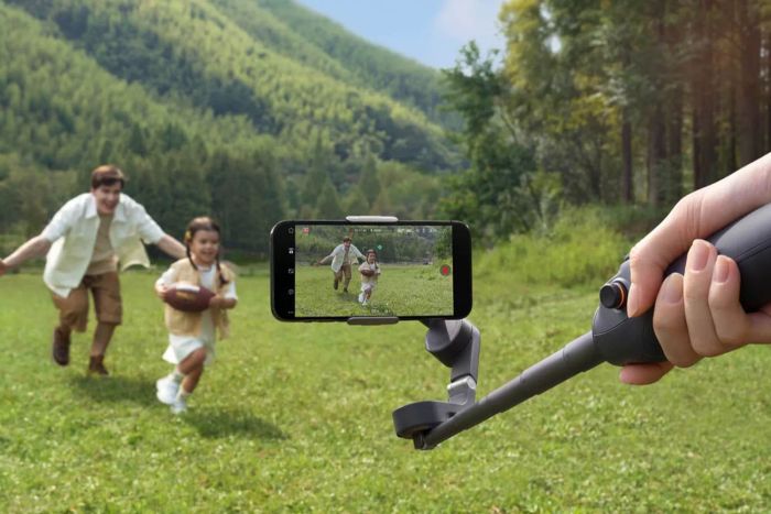 A DJI Osmo Mobile 6 Gimbal Stabilizer with a smartphone attached captures a man and a girl playing football on a grassy field