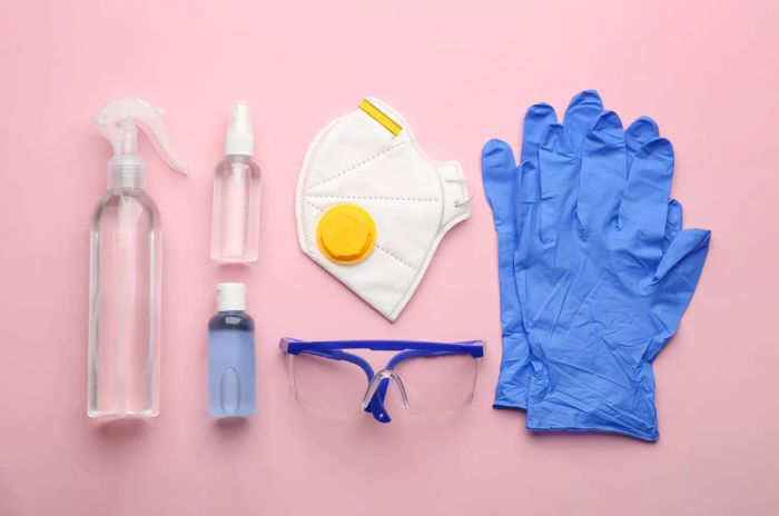 A flat lay arrangement featuring medical gloves, masks, and hand sanitizers on a pink background