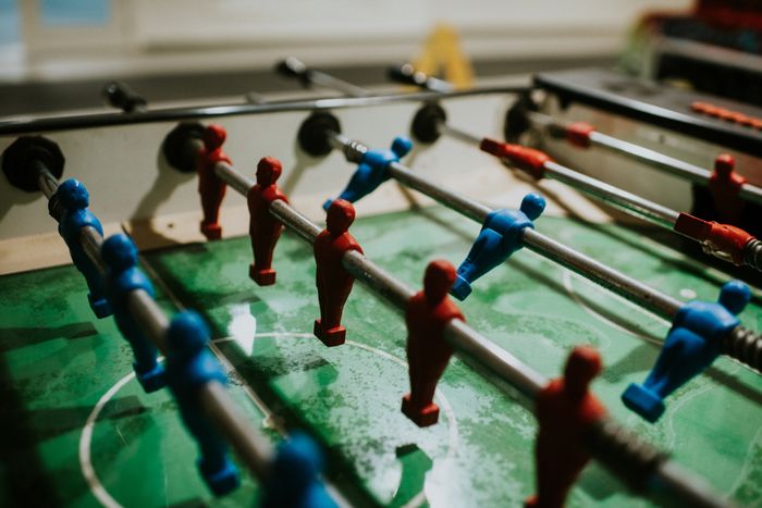 A foosball table with red and blue players positioned on metal rods, set against a green playing field.