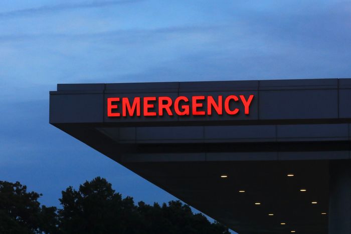 A glowing red emergency room entrance sign under a dim evening sky.