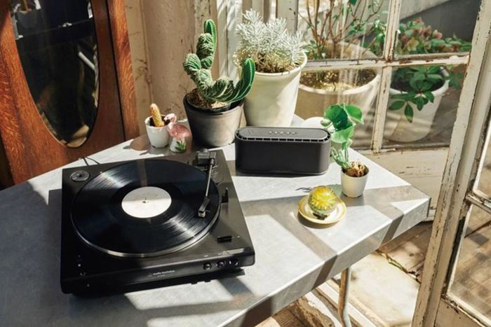 An Audio-Technica AT-LP60XBT Bluetooth Turntable sits elegantly on a metal table, surrounded by lush potted plants.