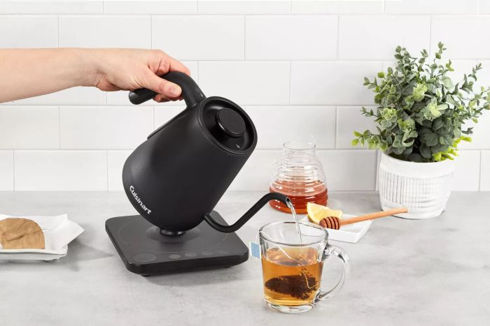 A person pours hot water from the Cuisinart GK-1 Digital Gooseneck Kettle into a glass of tea, ensuring a perfect brew.