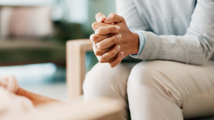 A person sitting in a therapy session, their hands folded thoughtfully as they engage with their therapist
