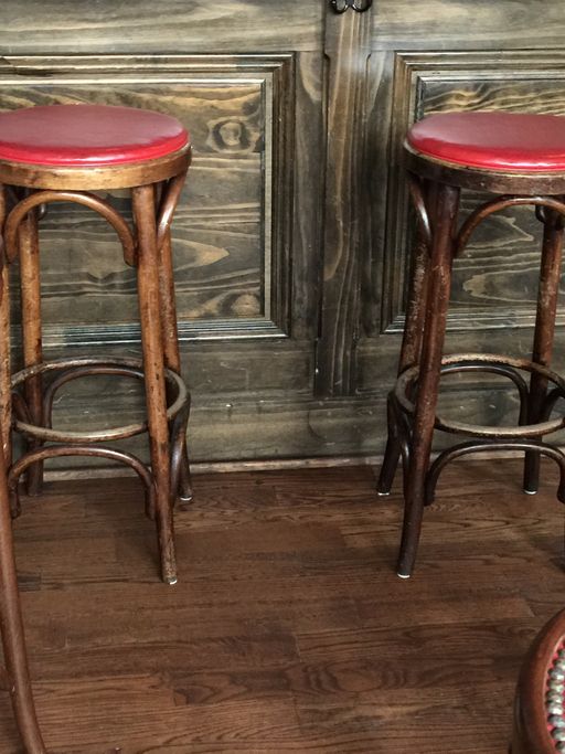 Two wooden bar stools with round seats rest on a wooden floor in front of a paneled wooden wall.