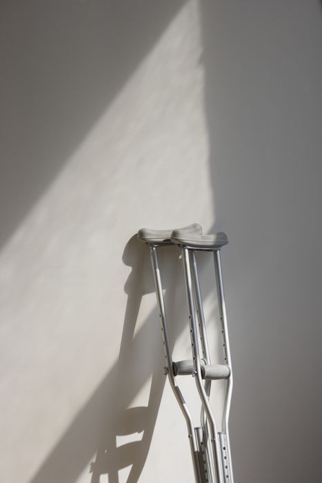 A pair of crutches is resting against a wall, their long shadows stretching across the floor.