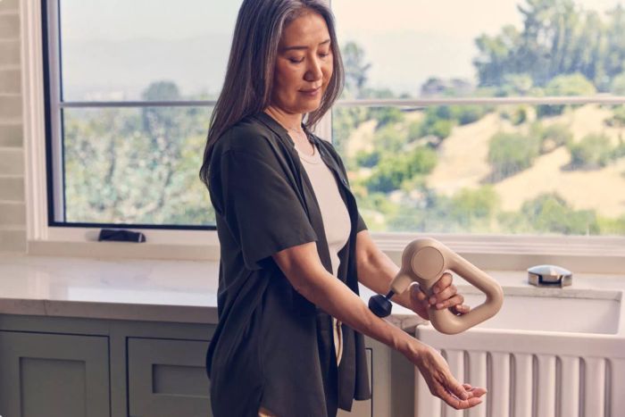 A person demonstrates using the Therabody Theragun Relief massage gun on their hand, soothing muscles and alleviating tension.