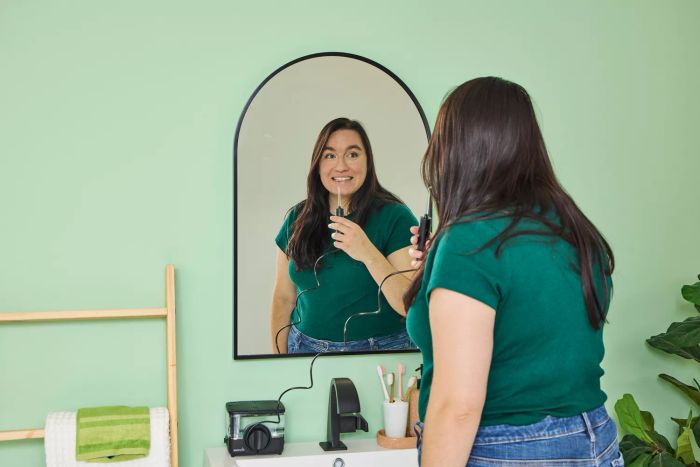 A user operating the Waterpik ION Professional Water Flosser while checking their reflection in a mirror