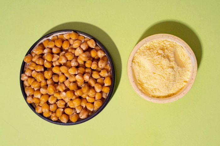 A bowl of chickpeas next to a bowl of chickpea flour on a green backdrop