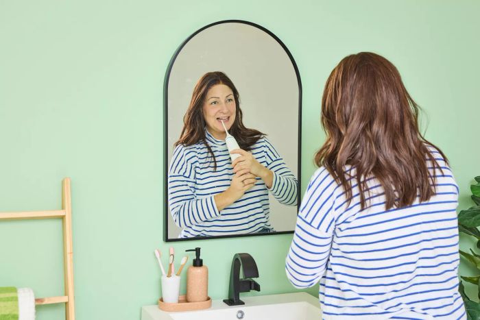 A user operating the Zima Dental Hydropod Smart Water Flosser at a sink while glancing into a mirror