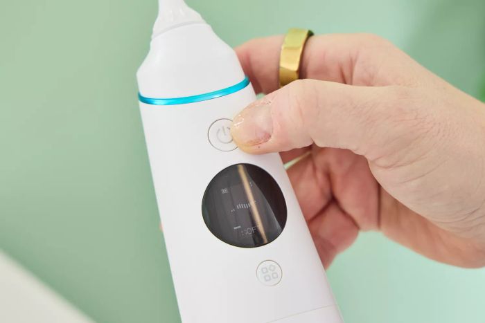 A thumb poised above the power button of the Zima Dental Hydropod Smart Water Flosser