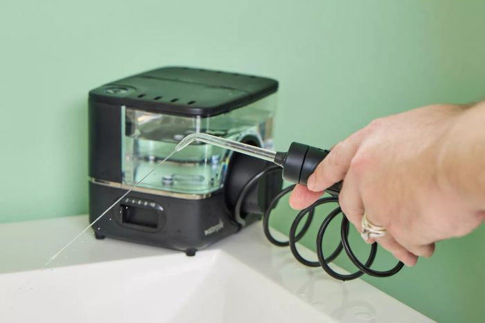 Two hands directing water from the Waterpik ION Professional Water Flosser into a sink