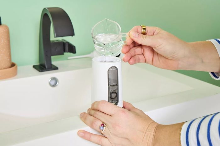 A user filling the water tank of the Zima Dental Hydropod Smart Water Flosser near a sink