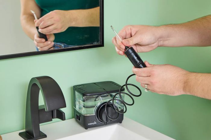A user holding a component of the Waterpik ION Professional Water Flosser near a sink