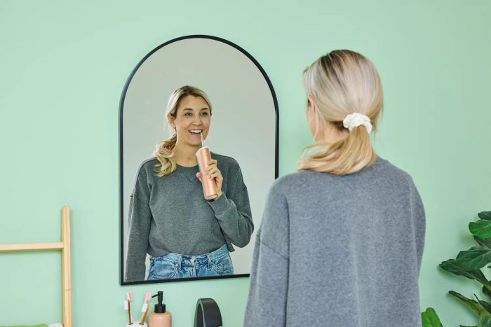 A user operating the Quip Rechargeable Cordless Water Flosser at a sink while checking their reflection in a mirror