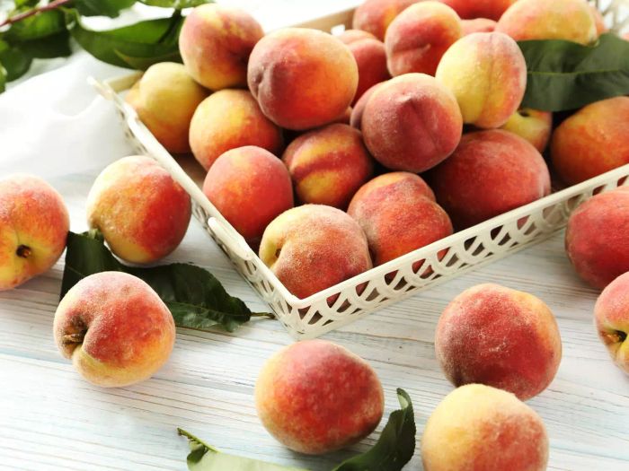 Fresh peaches arranged in a tray on a rustic white wooden table