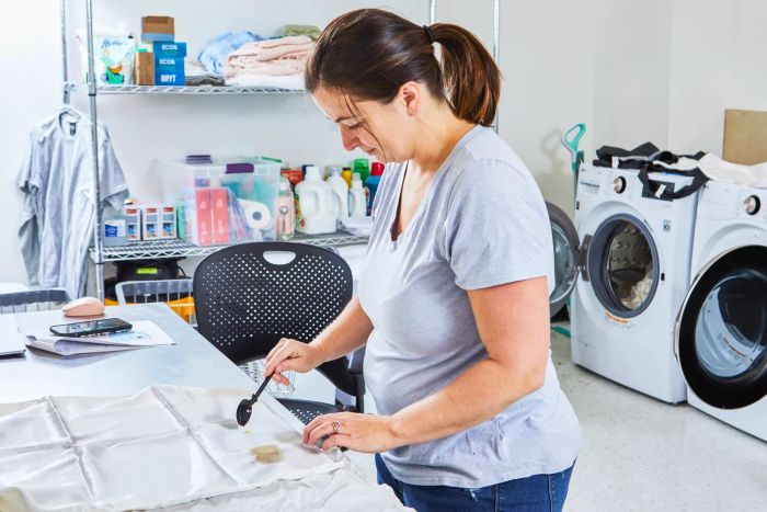 A person pouring liquid onto the Quince Mulberry Silk Sheet Set with laundry machines in the background