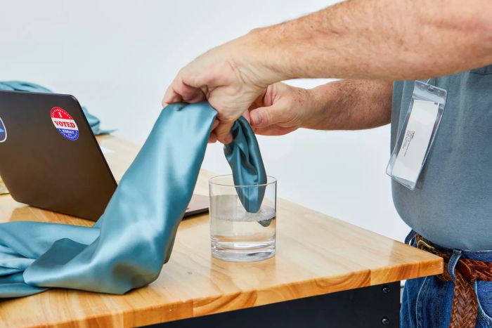 Person dipping a Colorado Home Co. Mulberry Silk Bed Sheets Set pillowcase into a glass of water