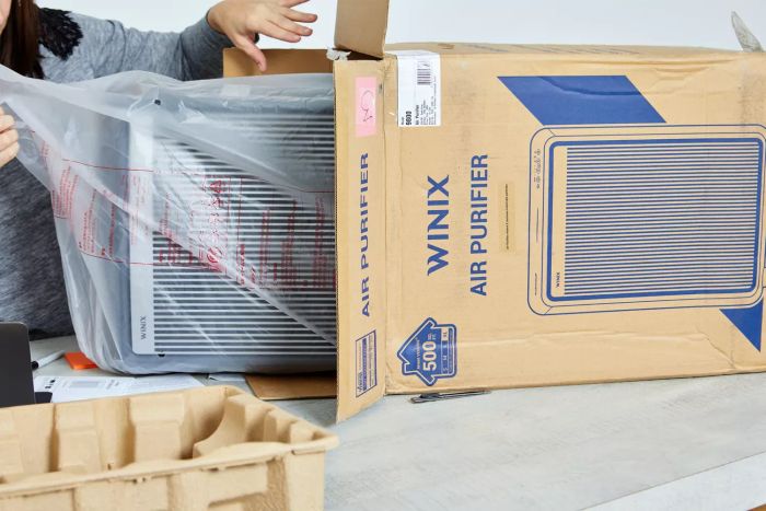 A person unboxing the Winix 9800 4-Stage True HEPA Air Purifier with WiFi & PlasmaWave Technology