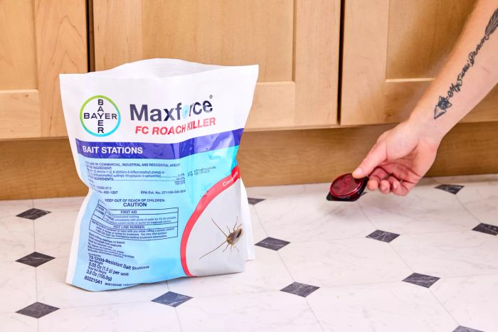 A hand setting a Maxforce FC Roach Killer Bait Station on a tile floor next to the product bag
