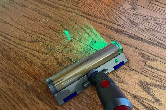 The Dyson Outsize+ Cordless Vacuum with a green light indicator, cleaning hair from a hardwood floor
