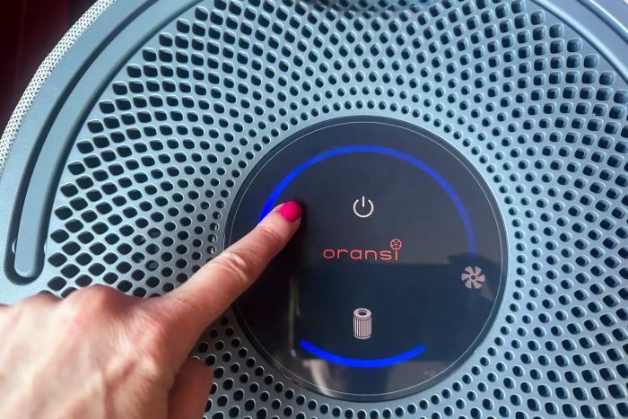 A person pressing a button on the Orsani Mod+ Hepa Air Filter