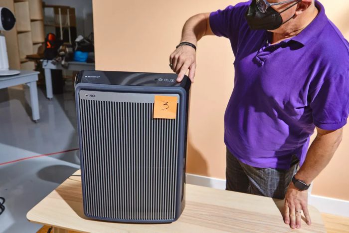 A person pressing a button on the Winix 9800 4-Stage True HEPA Air Purifier with WiFi & PlasmaWave Technology