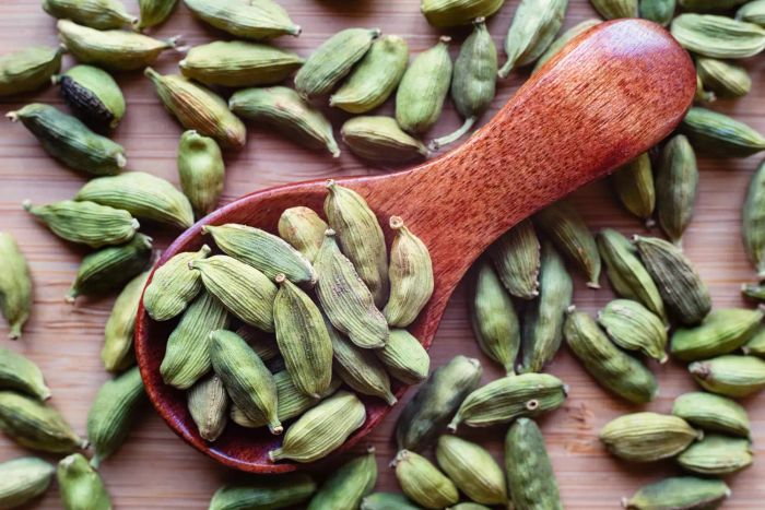 Dried cardamom pods resting on a wooden spoon, set against a rustic background.