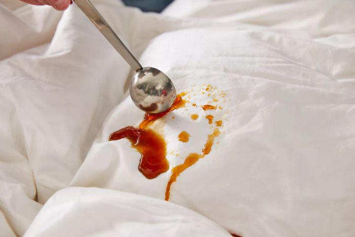 A spoon pouring brown liquid over the Feathered Friends Bavarian 700 Down Comforter