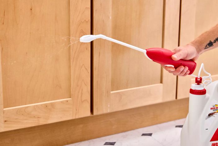 A hand applying the Ortho Home Defense Insect Killer near the cabinets