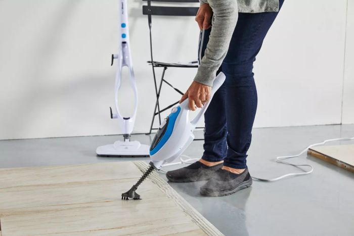 A person using the PurSteam 10-in-1 Steam Mop’s handheld attachment to clean a tiled floor.