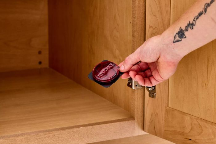 A hand positioning a Maxforce FC Roach Killer Bait Station inside a cabinet