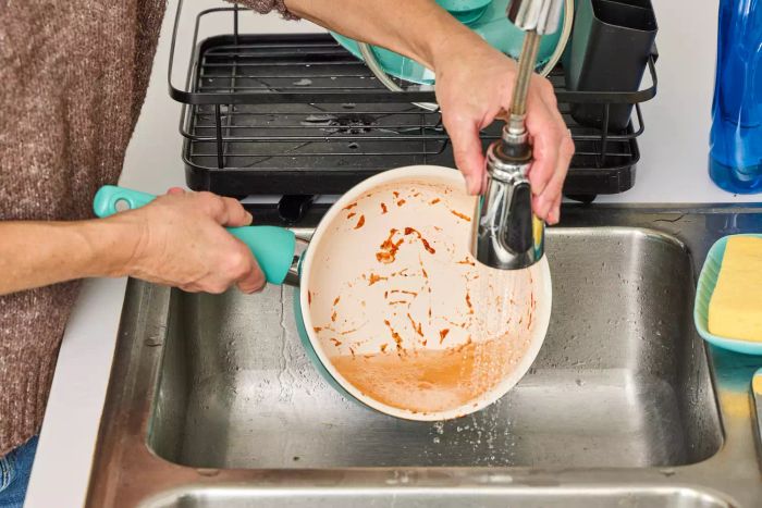 A person rinses a GreenPan Rio Ceramic Nonstick 16-Piece Cookware Set pot in the sink.
