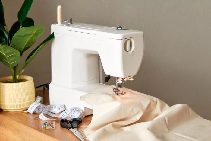 A workspace for a seamstress, featuring a sewing machine, a piece of natural beige cotton fabric, a measuring tape, scissors, and pins neatly arranged on a table.