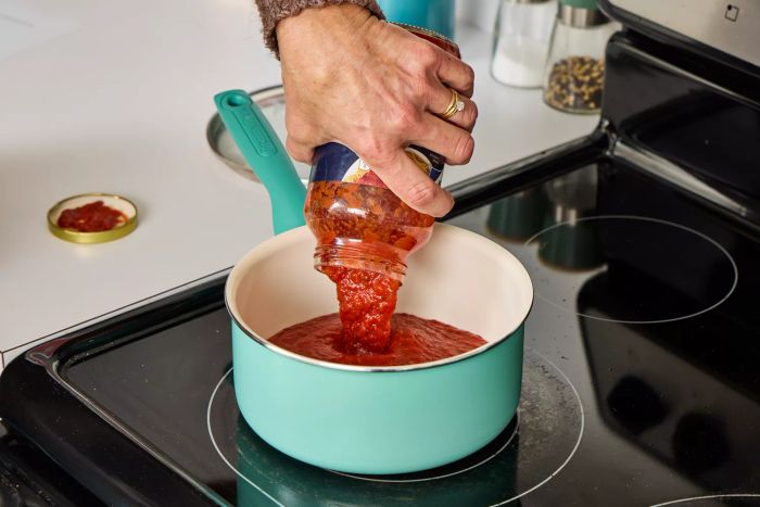 A person uses the GreenPan Rio Ceramic Nonstick 16-Piece Cookware Set to heat tomato sauce in a pot.