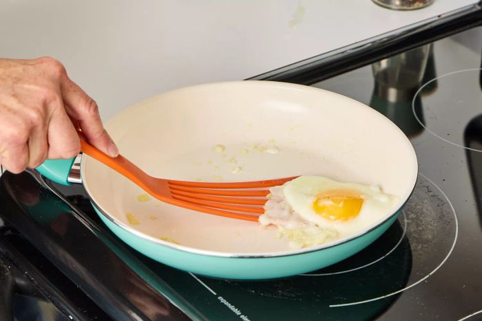 A person fries an egg in the GreenPan Rio Ceramic Nonstick 16-Piece Cookware Set pan.